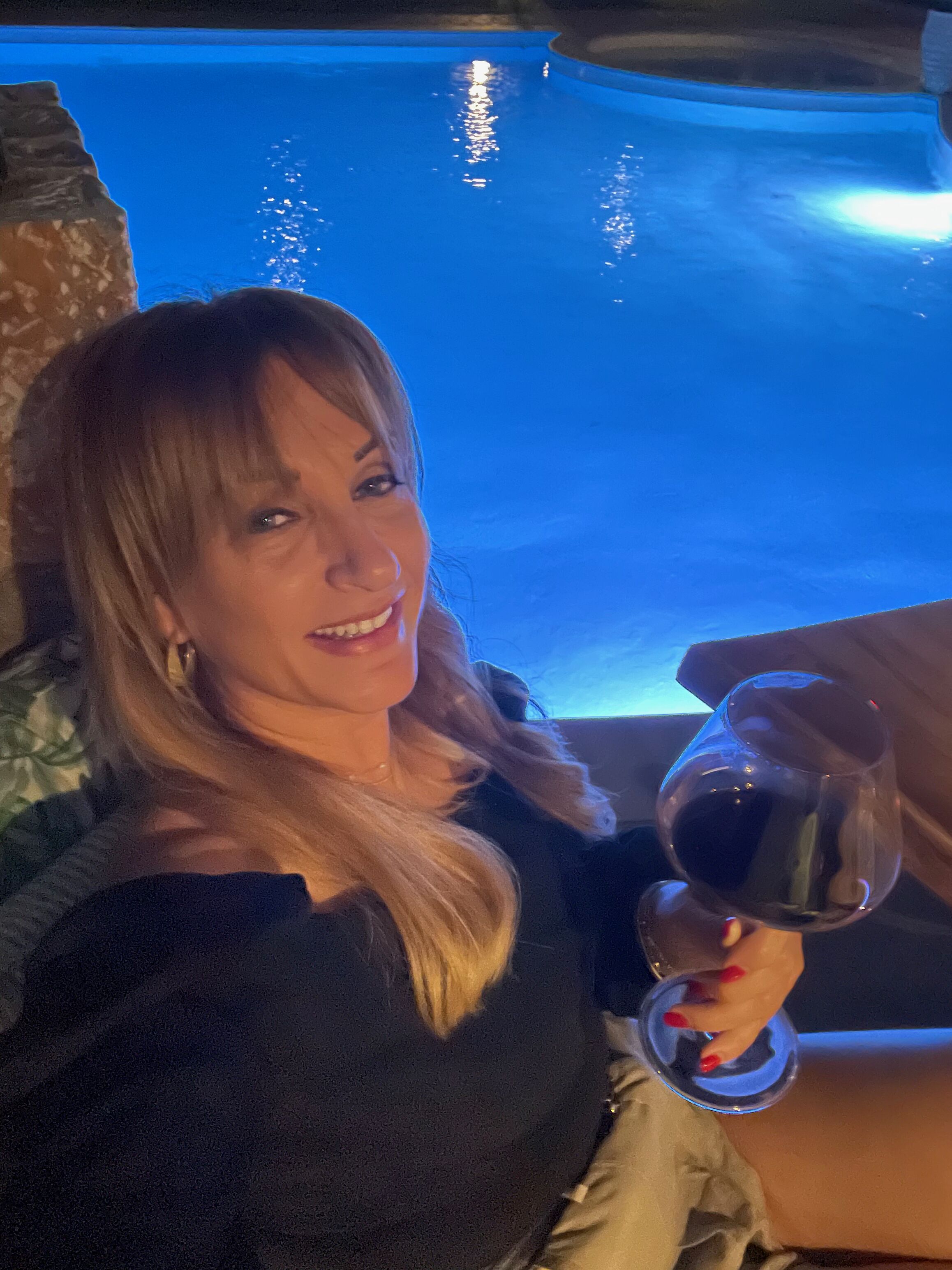 A person holding a glass of wine in a room with a pool in the background.