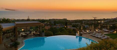 Un resort con una gran piscina, sillones de descanso y vistas al mar al atardecer.