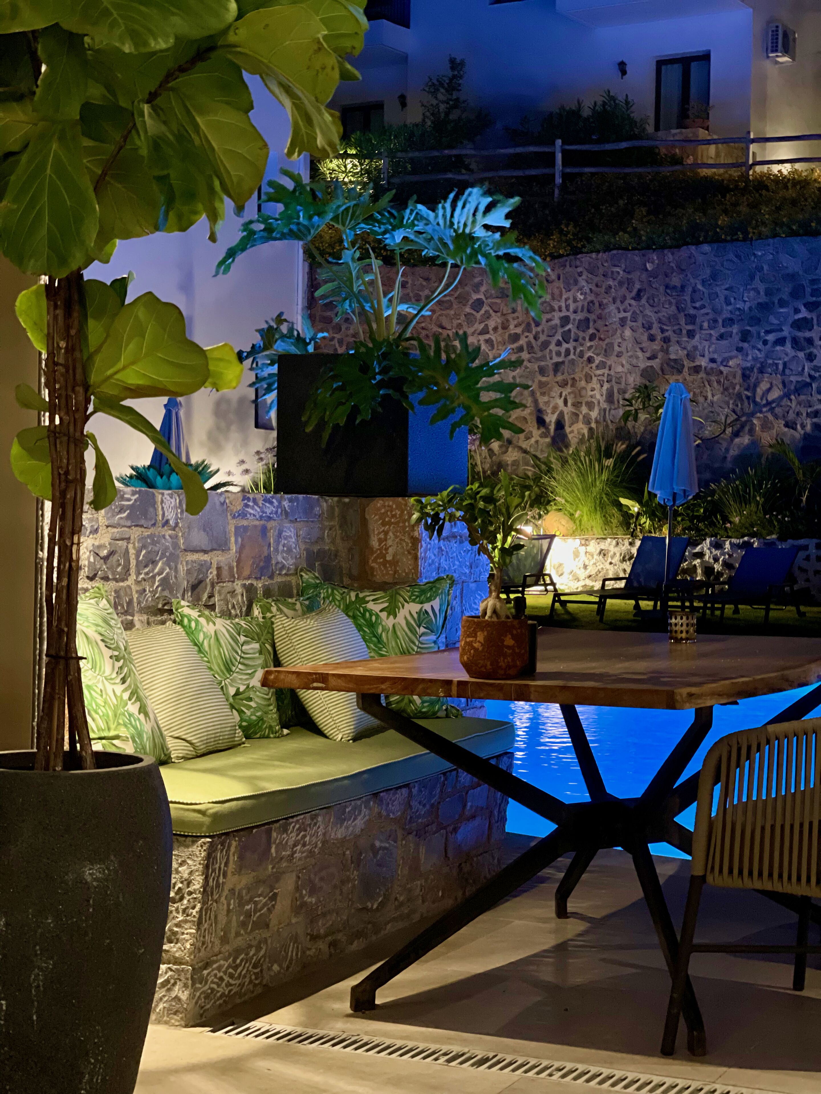 An outdoor pool area with stone walls, a wooden table, and lounge chairs.