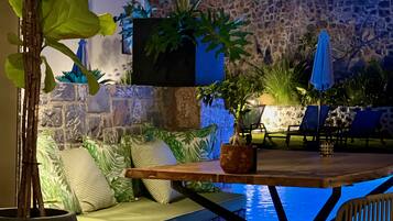 An outdoor pool area with stone walls, a wooden table, and lounge chairs.