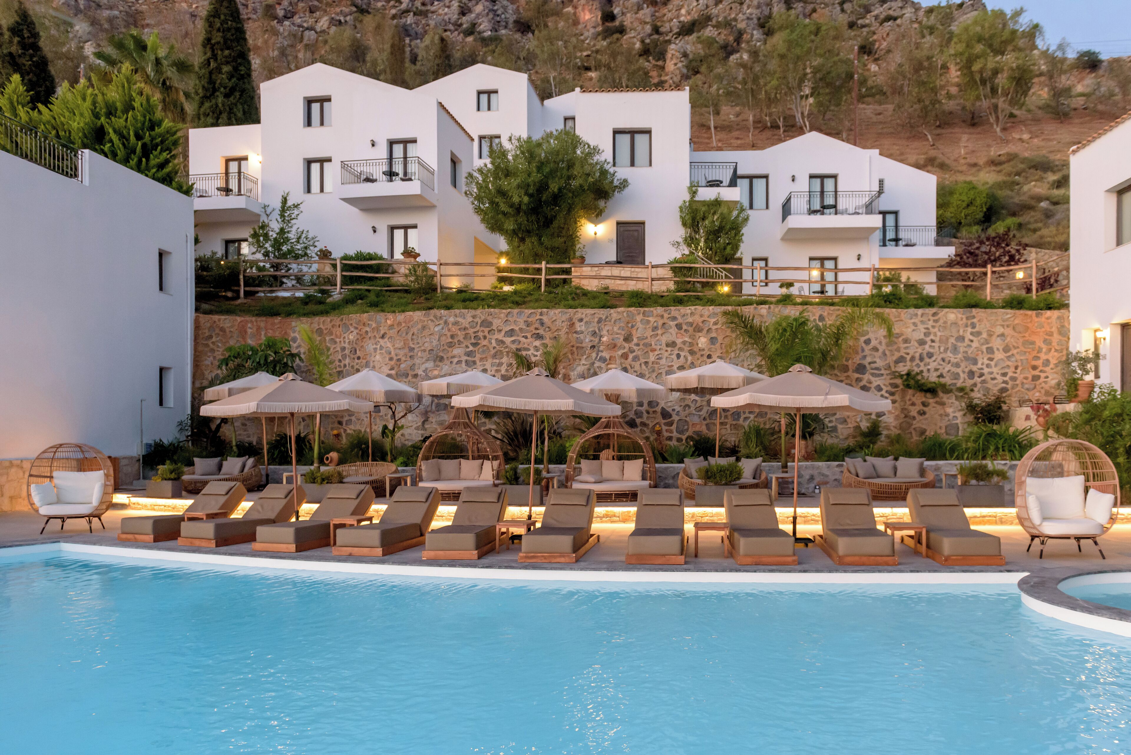A modern hotel with a pool area, lounge chairs, and umbrellas.