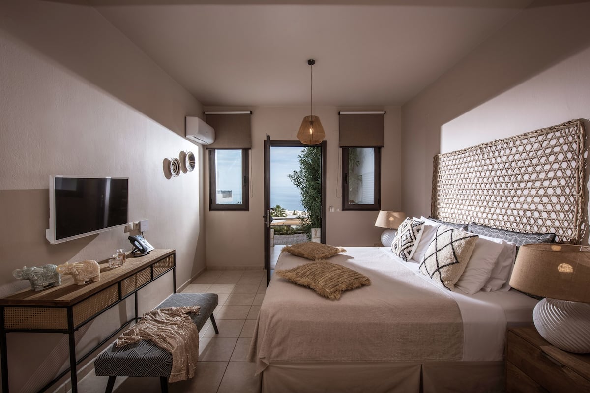 Un dormitorio con cama, mesitas de noche, televisor y vistas al exterior.