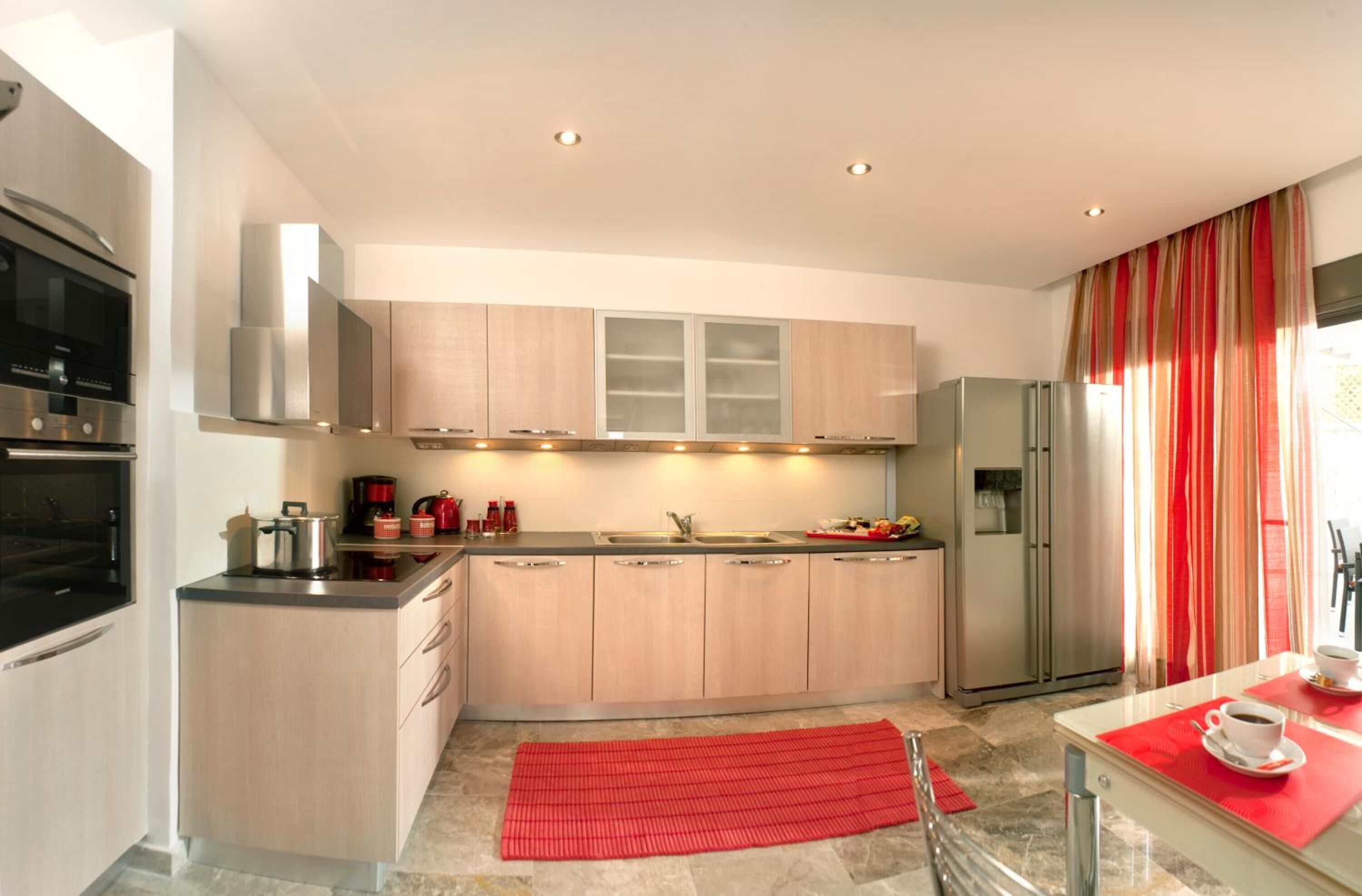 Una cocina moderna con electrodomésticos de acero inoxidable, una isla central y un comedor con un mantel individual rojo.