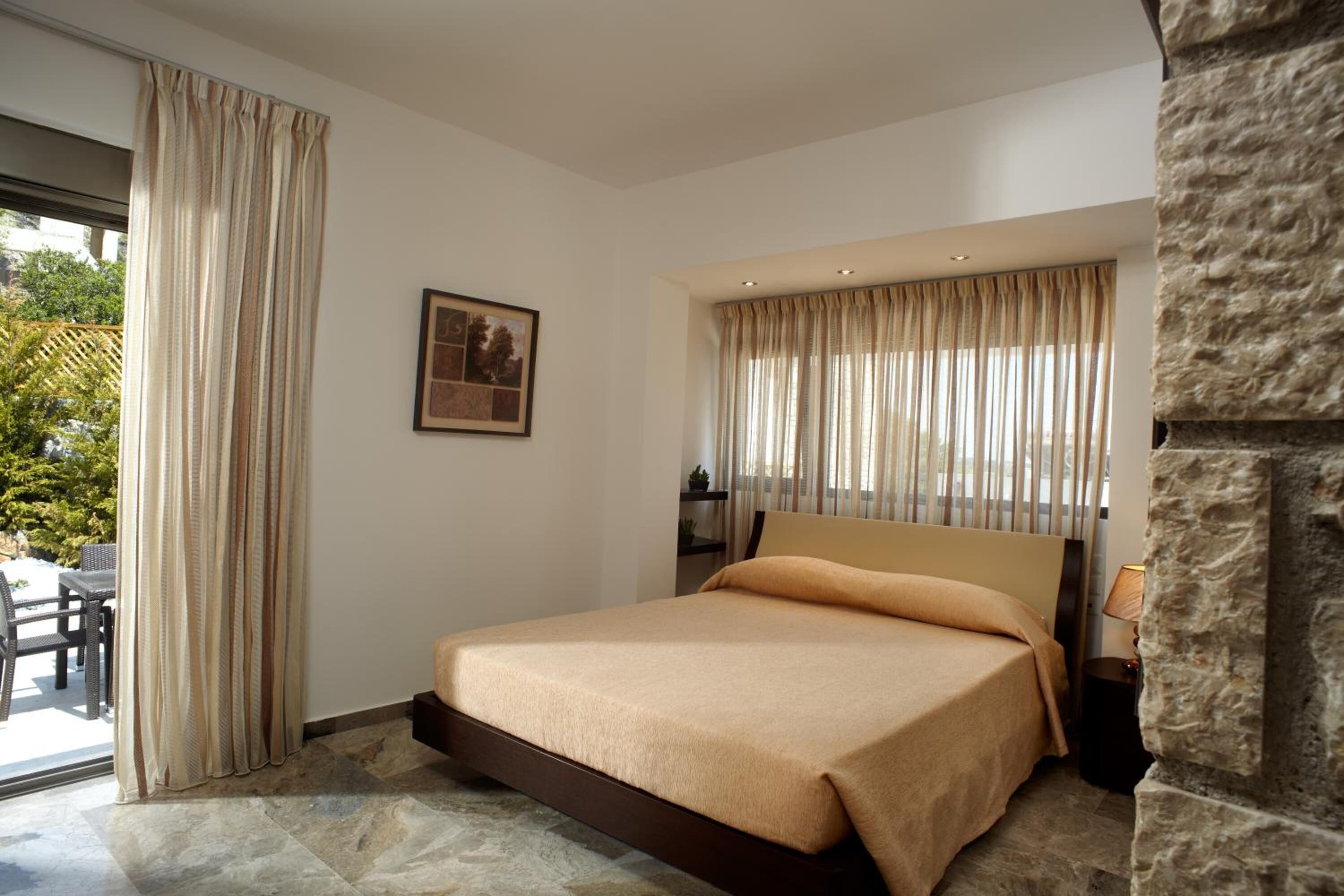 Un dormitorio con una cama grande, una pared de acento de piedra, una ventana con cortinas y vistas a la vegetación exterior.