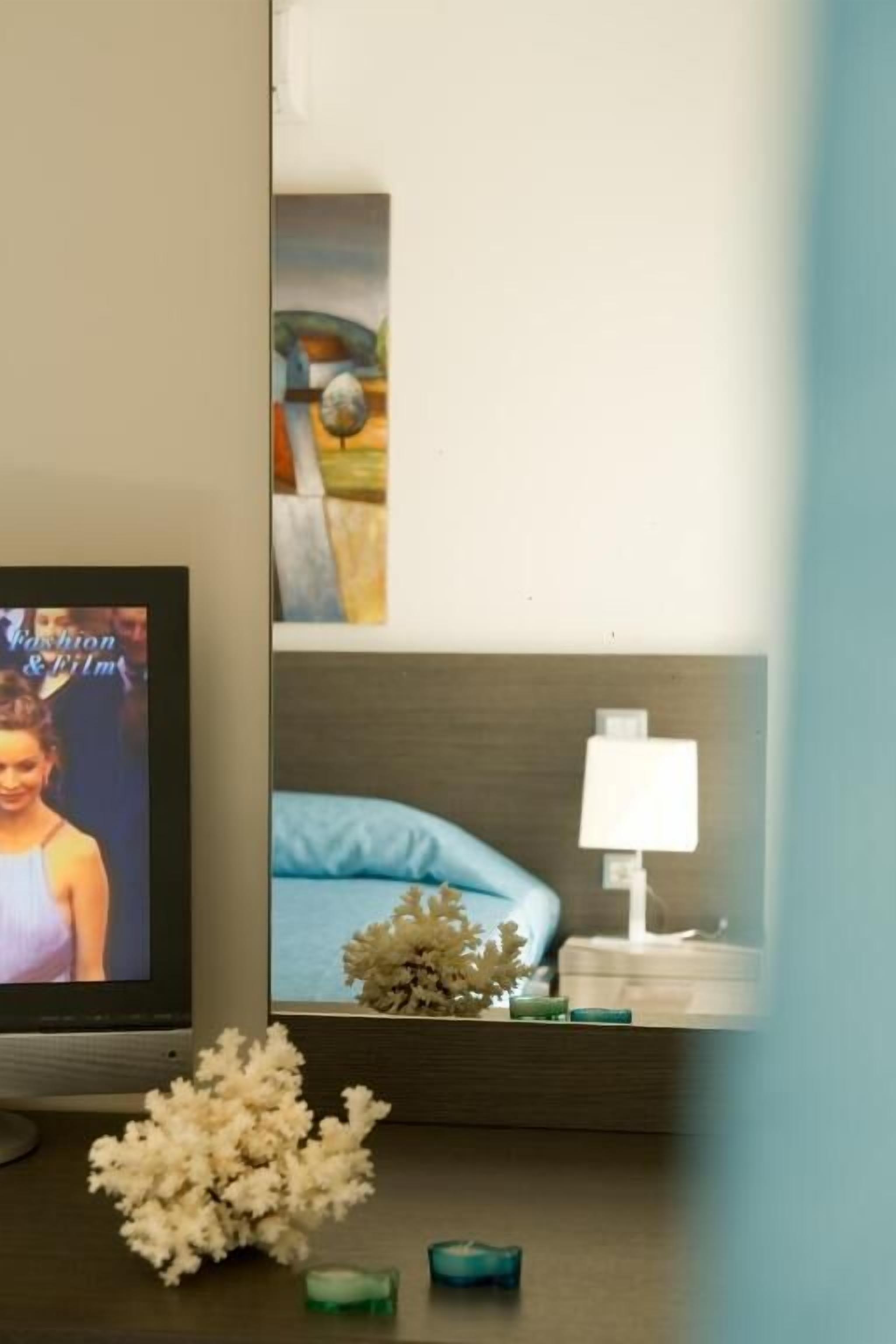Un téléviseur diffusant une émission de mode, une petite plante décorative et une table de chevet avec une lampe et un coussin bleu.