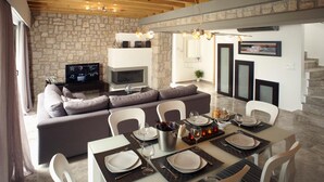 Ein modernes Wohnzimmer mit Steinwand, Kamin, Essbereich mit Tisch für vier Personen und einer Couch.