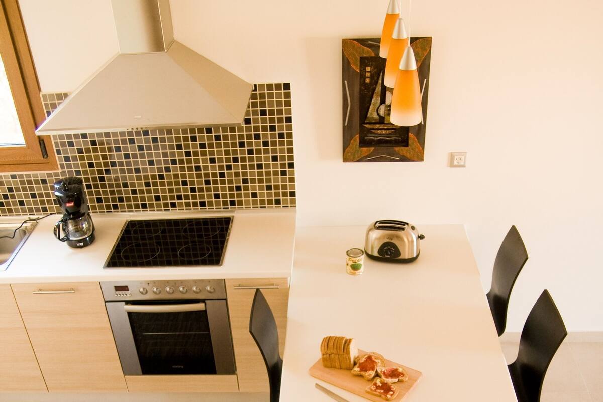 Een moderne keuken met een wit aanrecht, roestvrijstalen apparatuur en een eethoek met een witte tafel en zwarte stoelen.