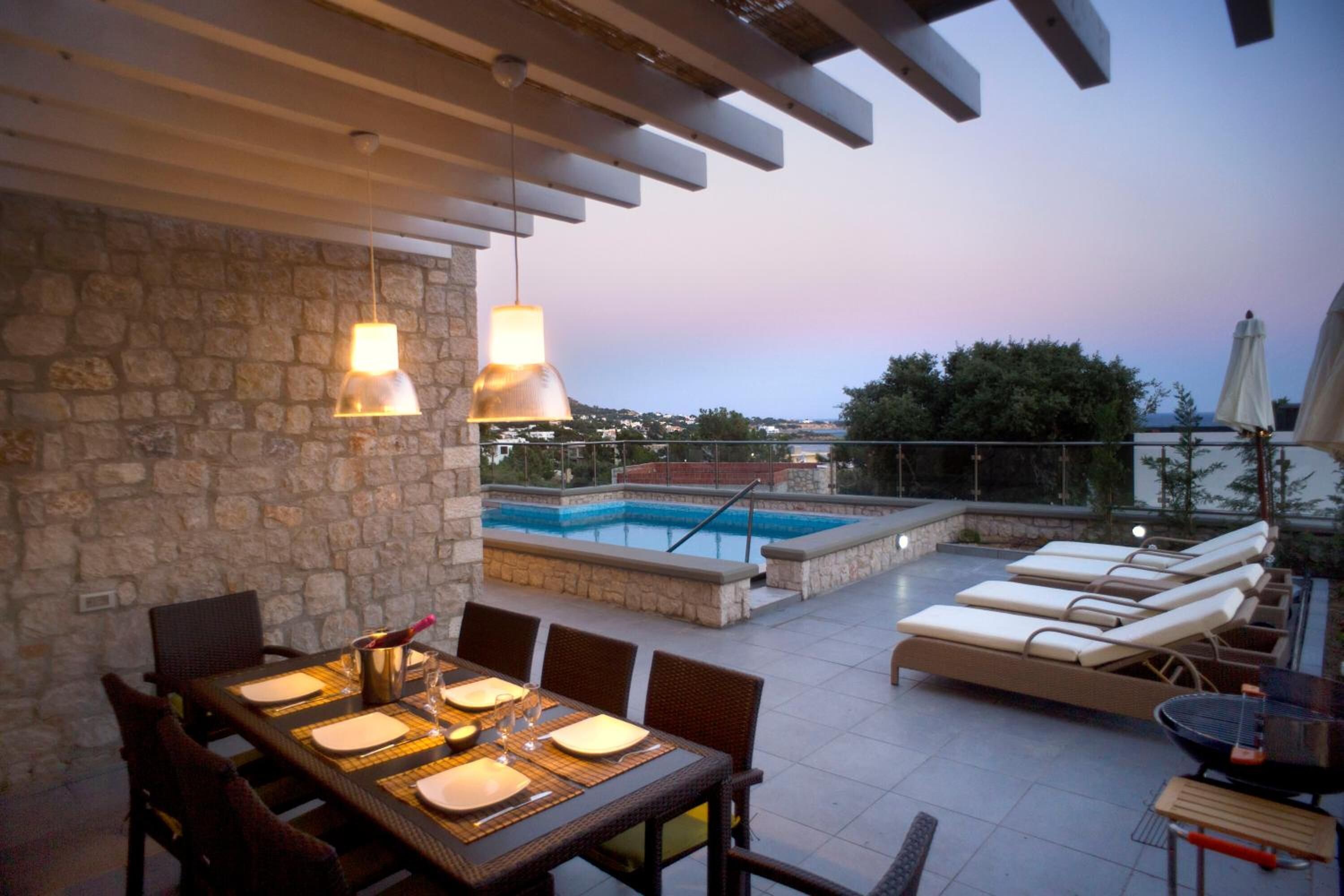 An outdoor dining area with a stone wall, a pool, and lounge chairs.