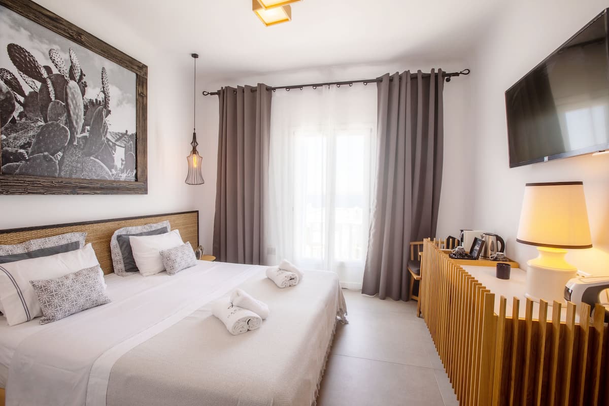 Hotellihuone, jossa on suuri sänky, taulutelevisio, yöpöytä lampun kanssa ja ikkuna, jossa on verhot.