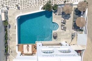 Vista aérea de un hotel con una amplia piscina, tumbonas, sombrillas y un bar en la azotea.