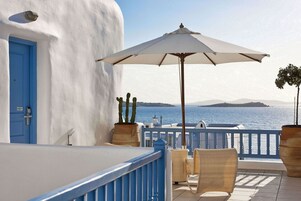 Un balcón con una pared blanca, una puerta azul y vista al mar.