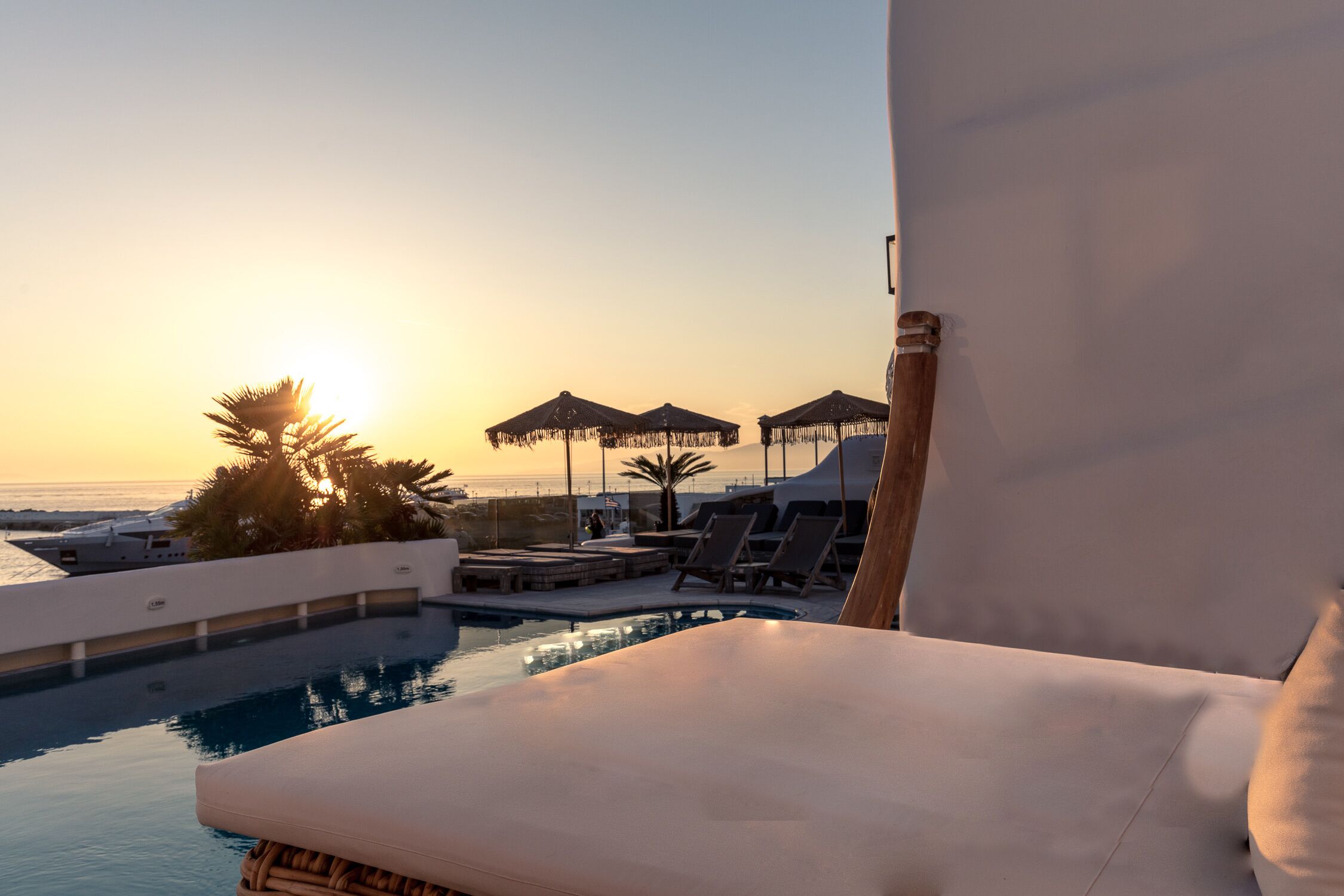 A poolside area with lounge chairs, umbrellas, and a view of the sunset over the ocean.