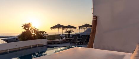 A poolside area with lounge chairs, umbrellas, and a view of the sunset over the ocean.