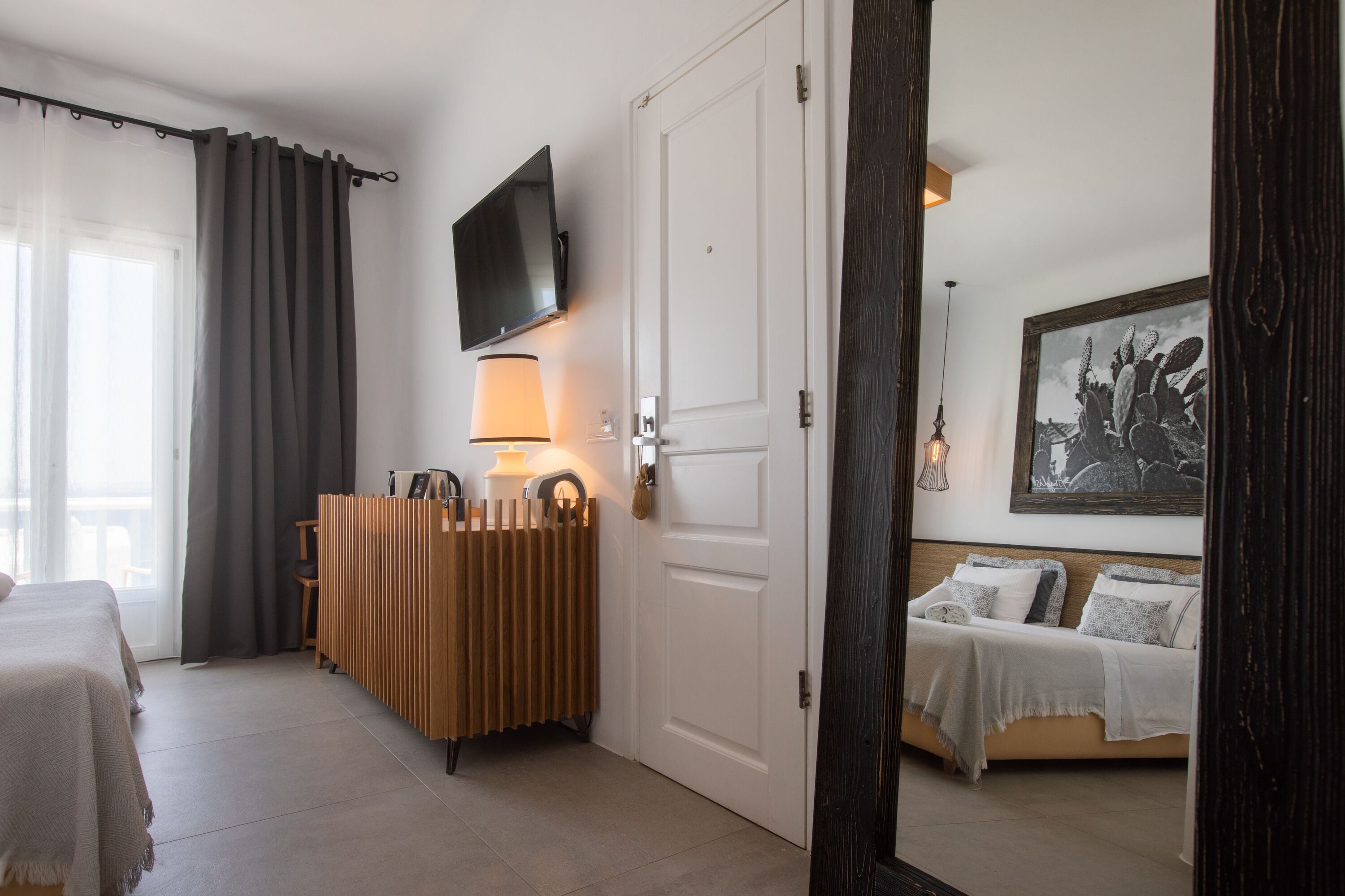 A hotel room with a bed, a bedside table, a lamp, a radiator, a TV mounted on the wall, and a framed picture on the wall.