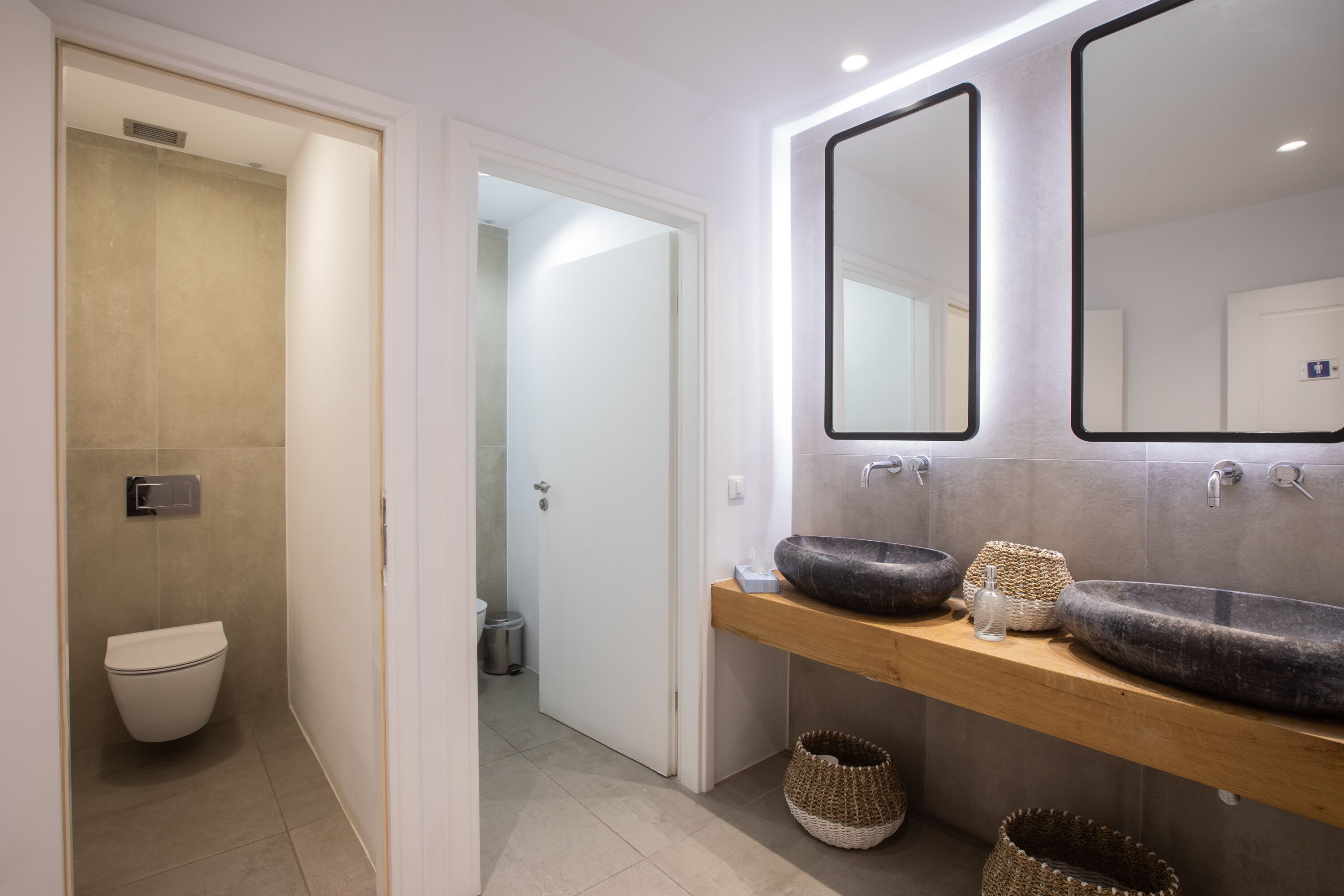 Ein modernes Badezimmer mit Toilette, zwei Waschbecken und einem Spiegel.