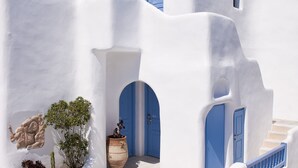 Un edificio blanco con puertas y ventanas azules, piso de piedra y una planta de cactus.