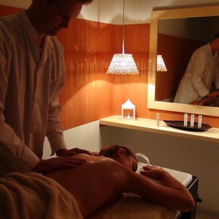 A massage therapy room with a wooden wall, a mirror, and a shelf with candles and flowers.
