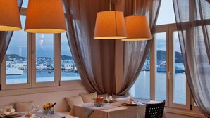 Un comedor con una mesa dispuesta para dos, ventanas amplias con cortinas y vista al puerto.