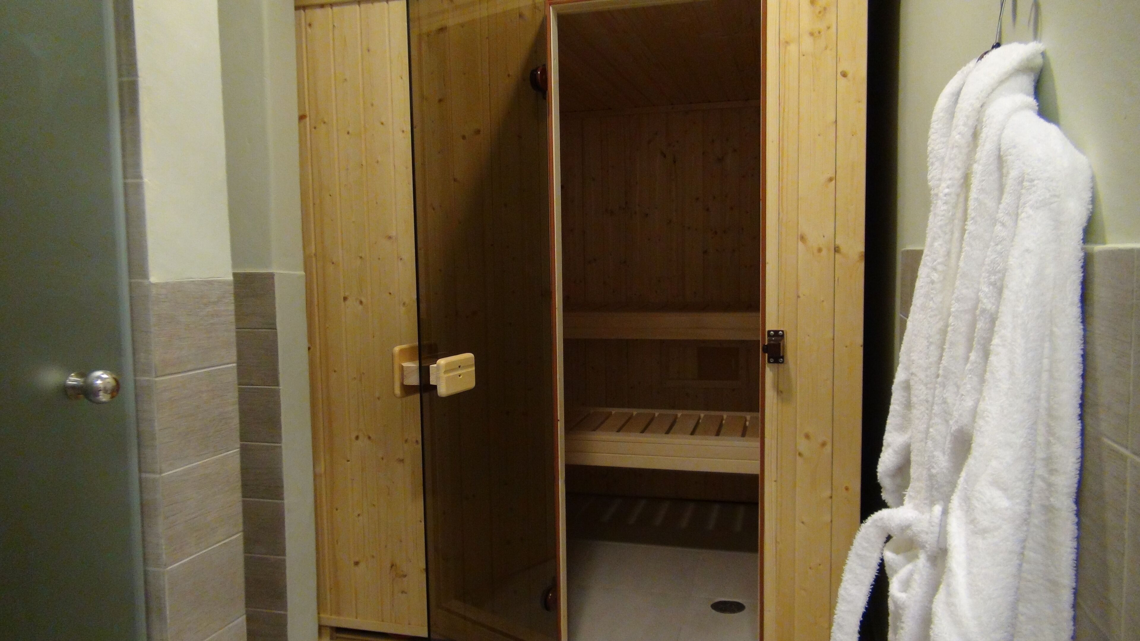 A wooden sauna room with a bench, a towel hanging on the wall, and a door leading to another room.