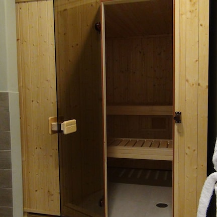 A wooden sauna room with a bench, a towel hanging on the wall, and a door leading to another room.