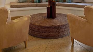 Un salón con sofá, dos sillones, una mesa de centro redonda, lámpara colgante, ventana con persianas y decoraciones de esqueletos de peces en la pared.