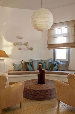 A living room with a sofa, two armchairs, a round coffee table, a hanging light fixture, a window with blinds, and wall-mounted fish skeleton decorations.