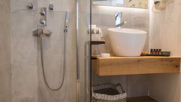 A modern bathroom with a glass-enclosed shower, a large white sink, and a wooden shelf with toiletries.