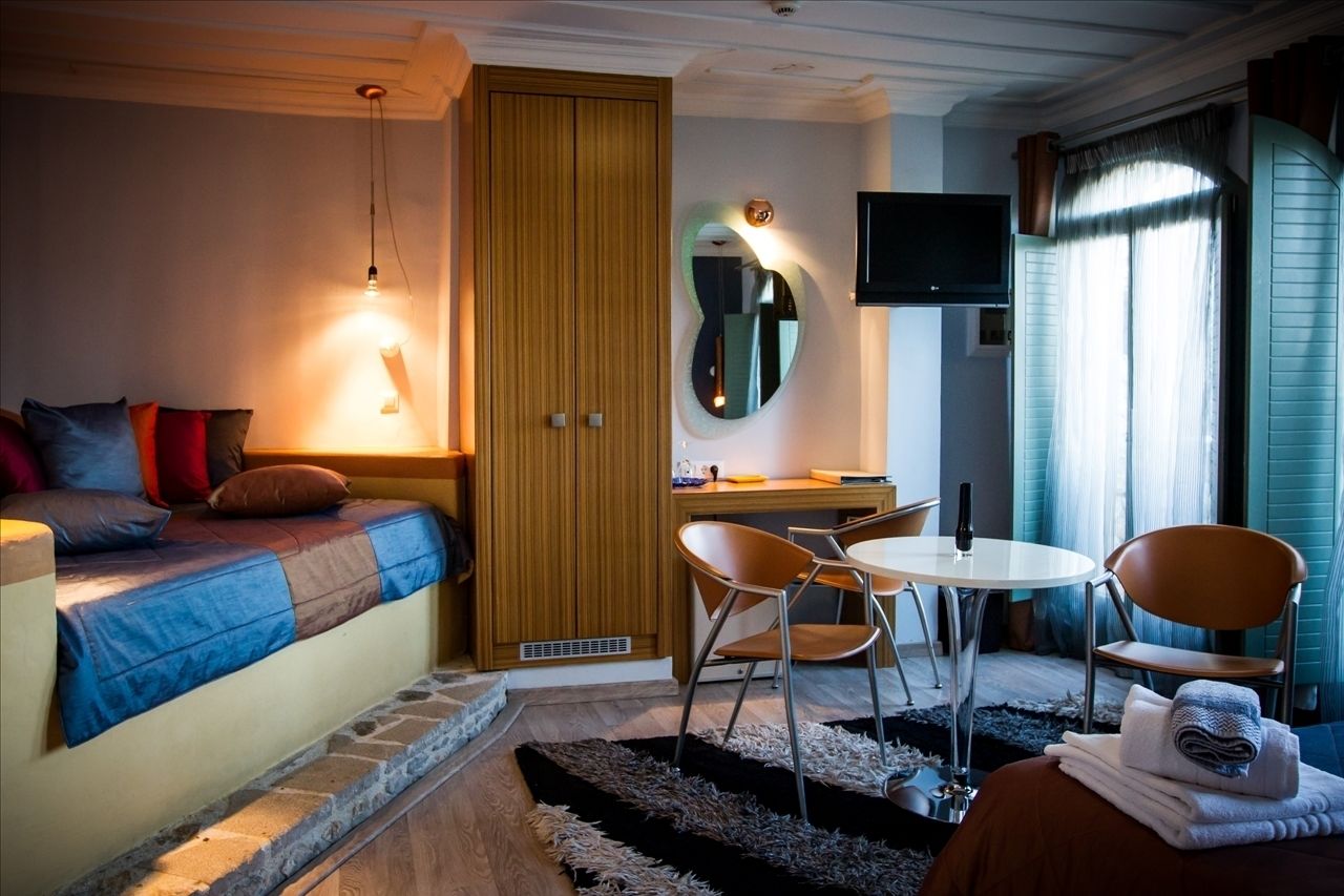 Habitación de hotel con una cama, un escritorio, dos sillas, un televisor y un espejo.