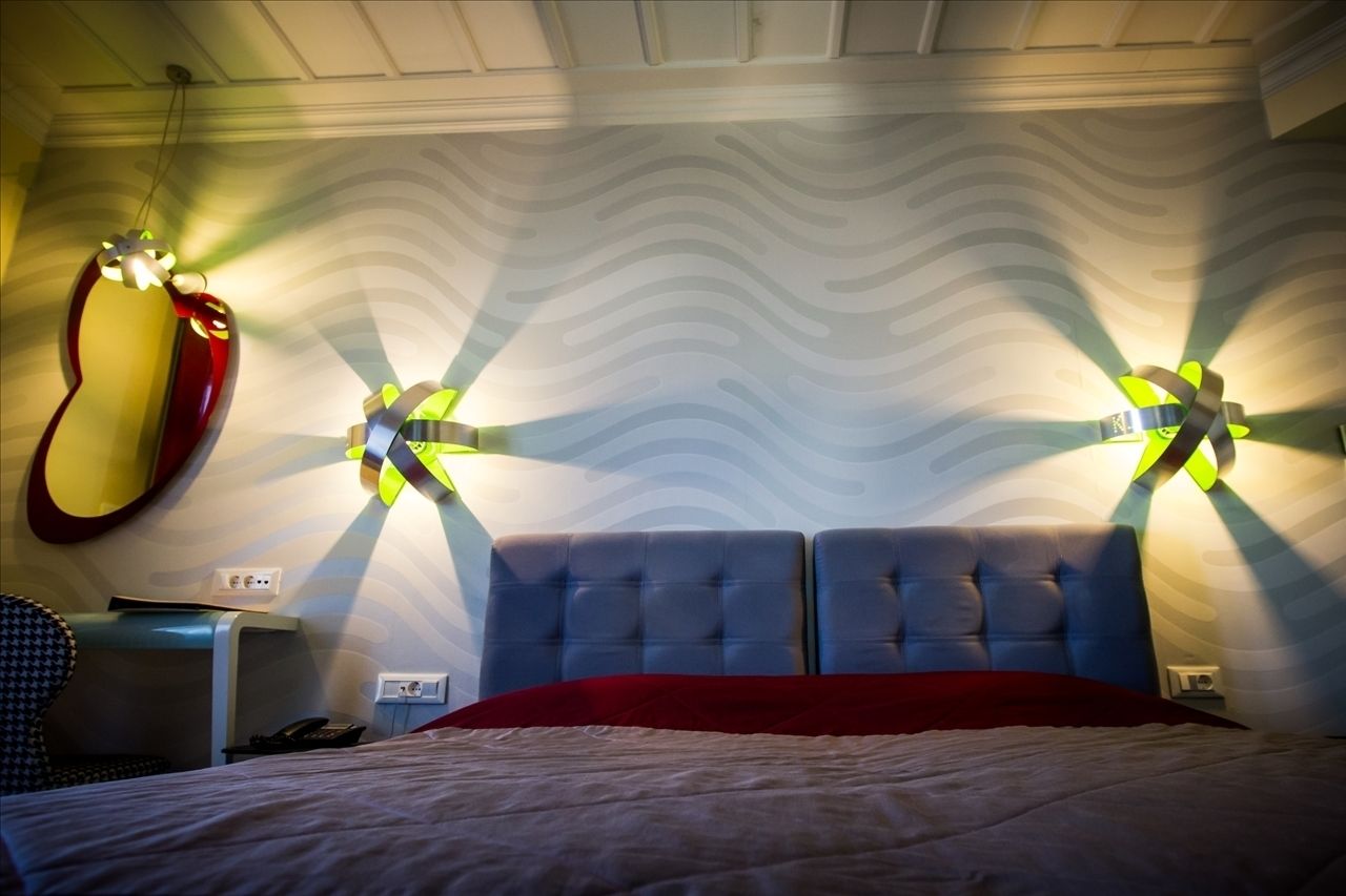 A hotel room with a tufted headboard, a red bedspread, and a wall with a wavy pattern.