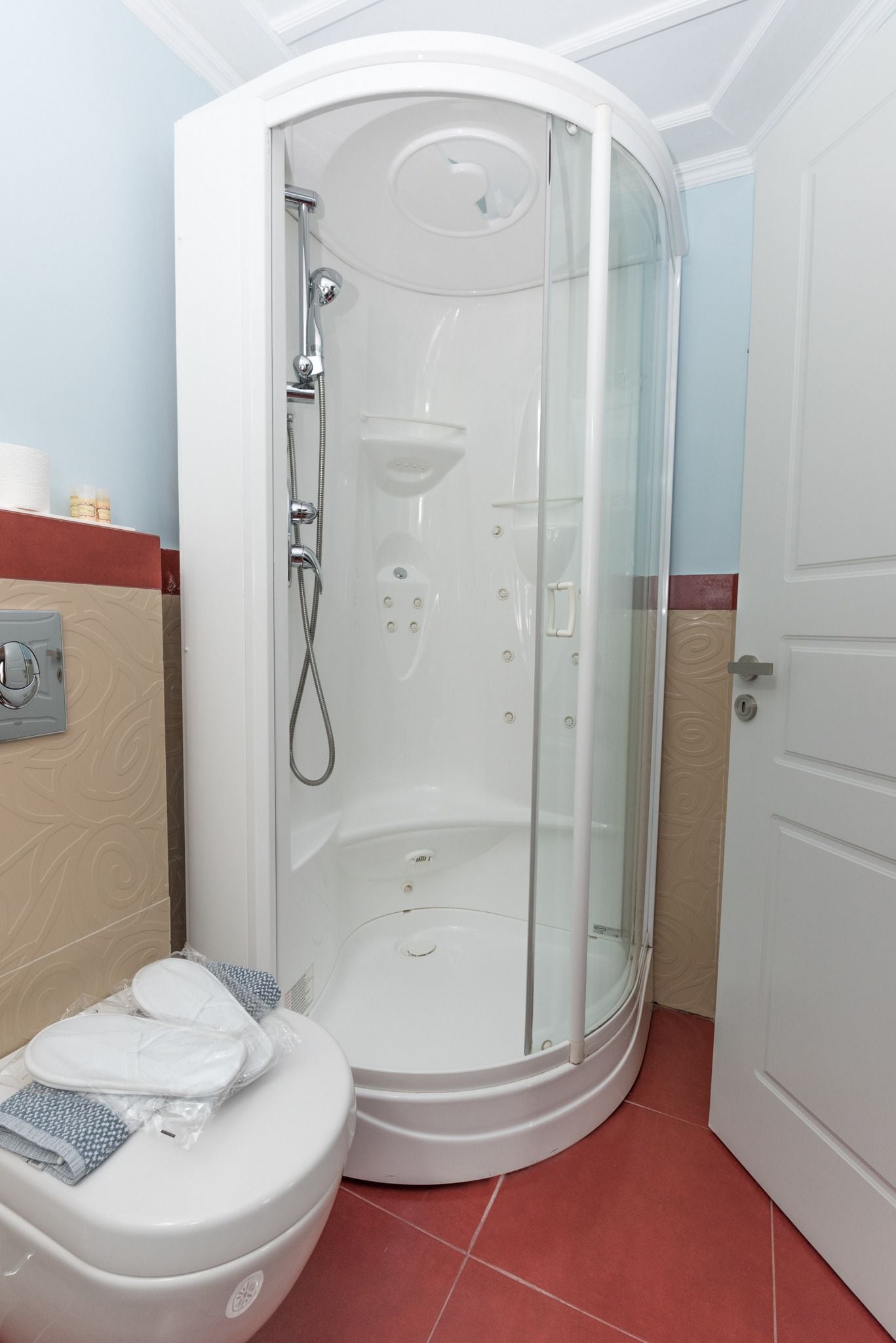 A modern bathroom with a glass-enclosed shower, a white toilet, and a red-tiled floor.