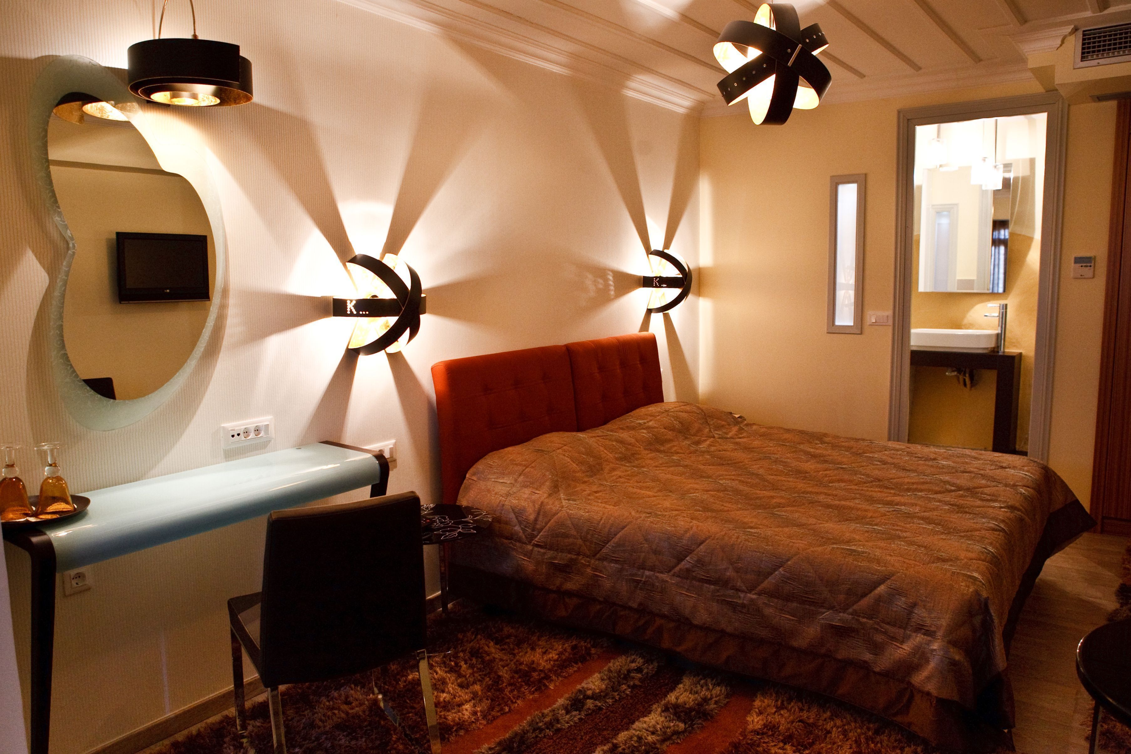 A bedroom with a bed, a desk, a chair, a mirror, and a bathroom visible through an open door.