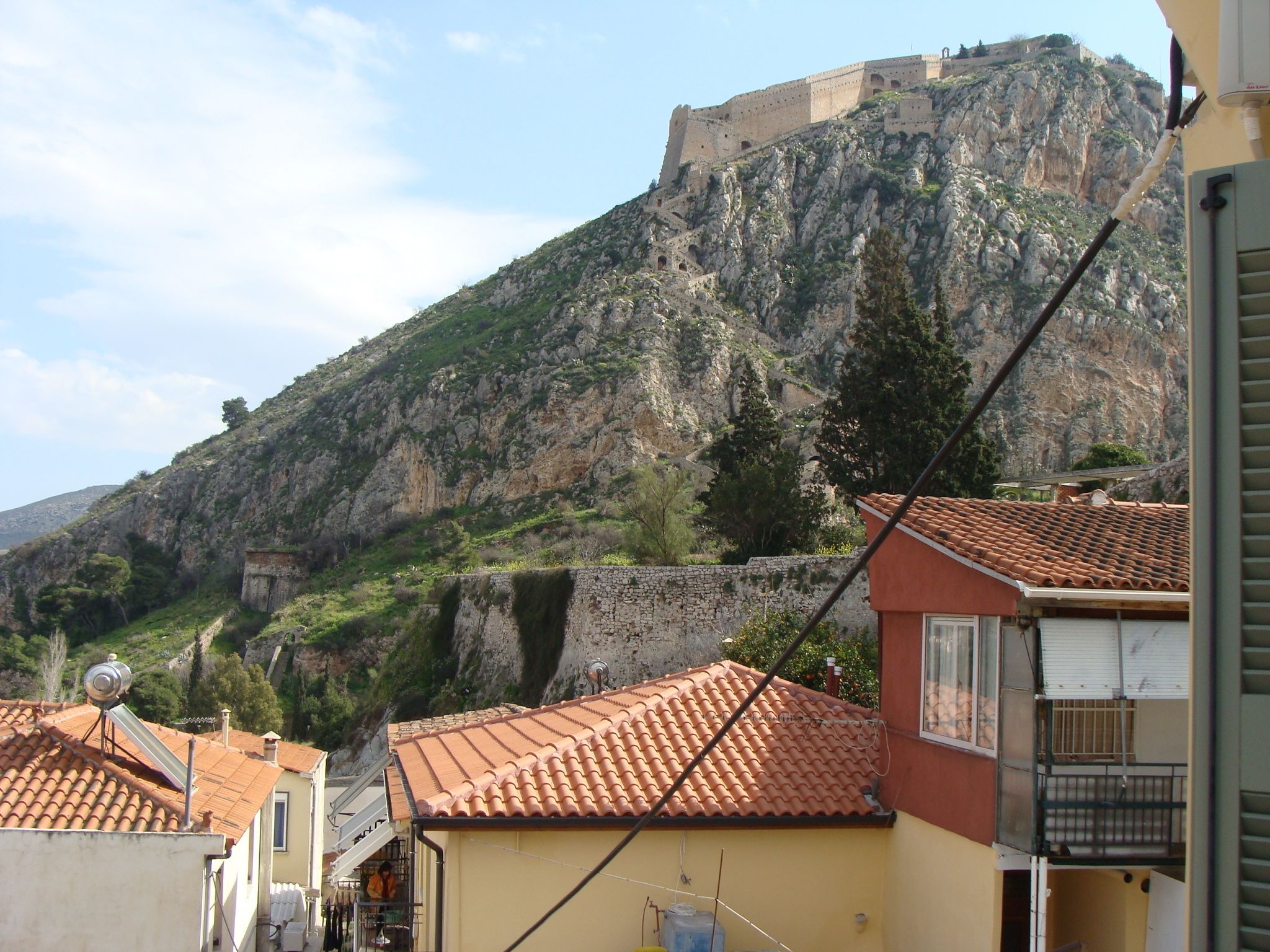 A building with a tiled roof, a stone wall, and a view of a fort on a hill.
