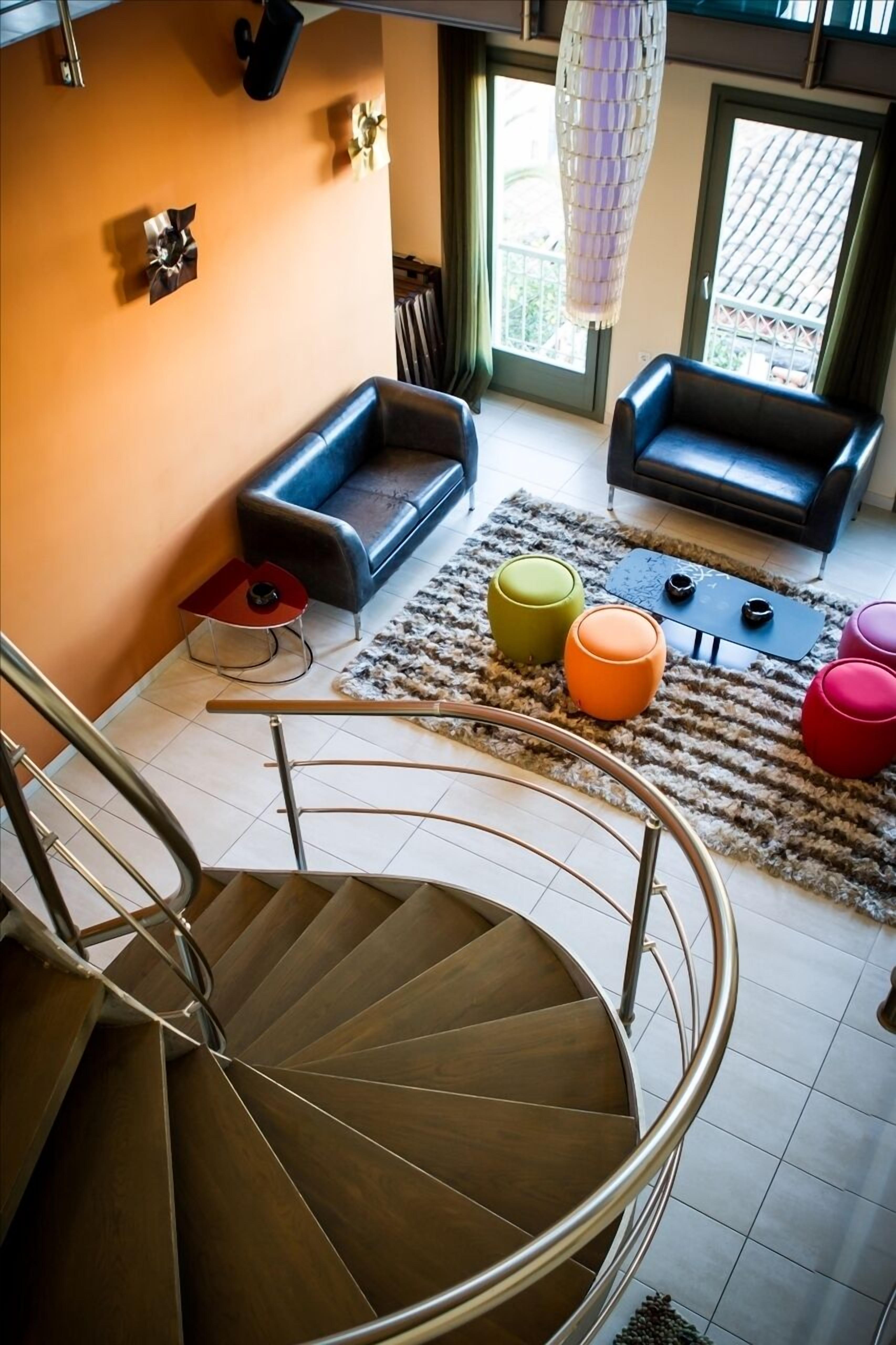 Una sala de estar moderna con una escalera en espiral, dos sofás, otomanas coloridas y una alfombra estampada.