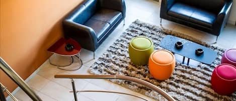Una sala de estar moderna con una escalera en espiral, dos sofás, otomanas coloridas y una alfombra estampada.