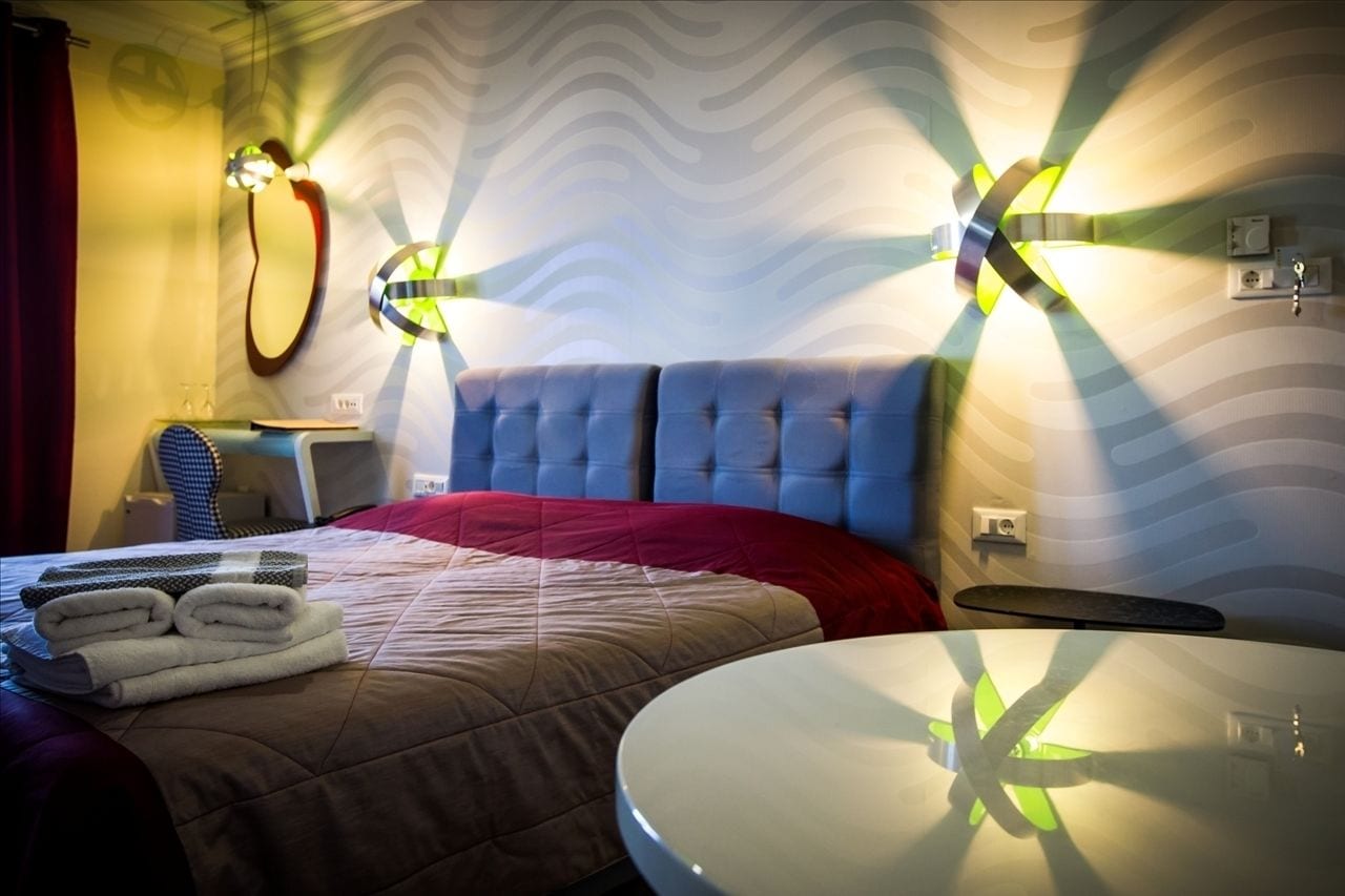 A hotel room with a tufted headboard, a round table, and a bed with a red blanket and folded towels.