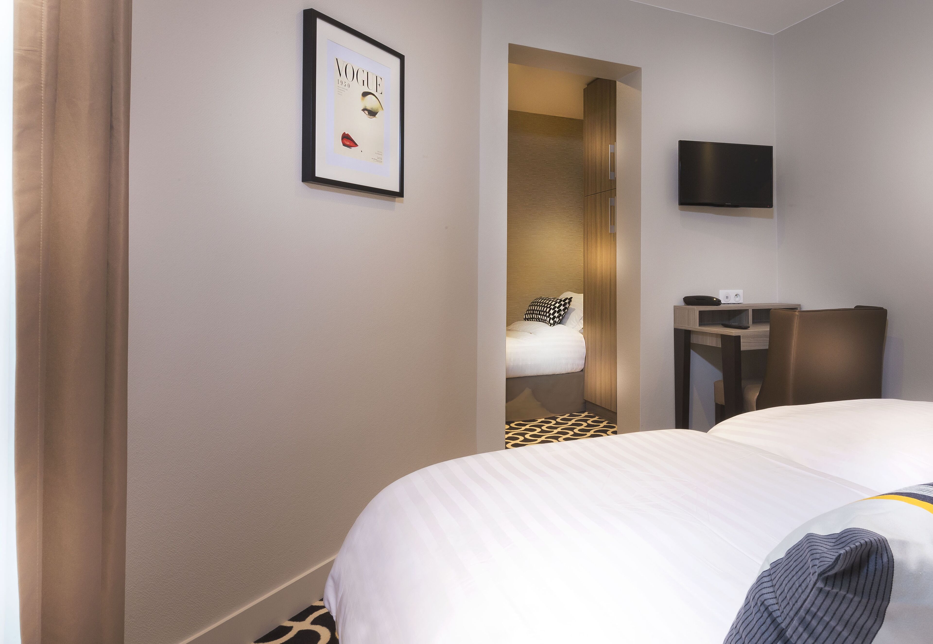 A hotel room with a bed, a desk, a television, and a framed picture on the wall.