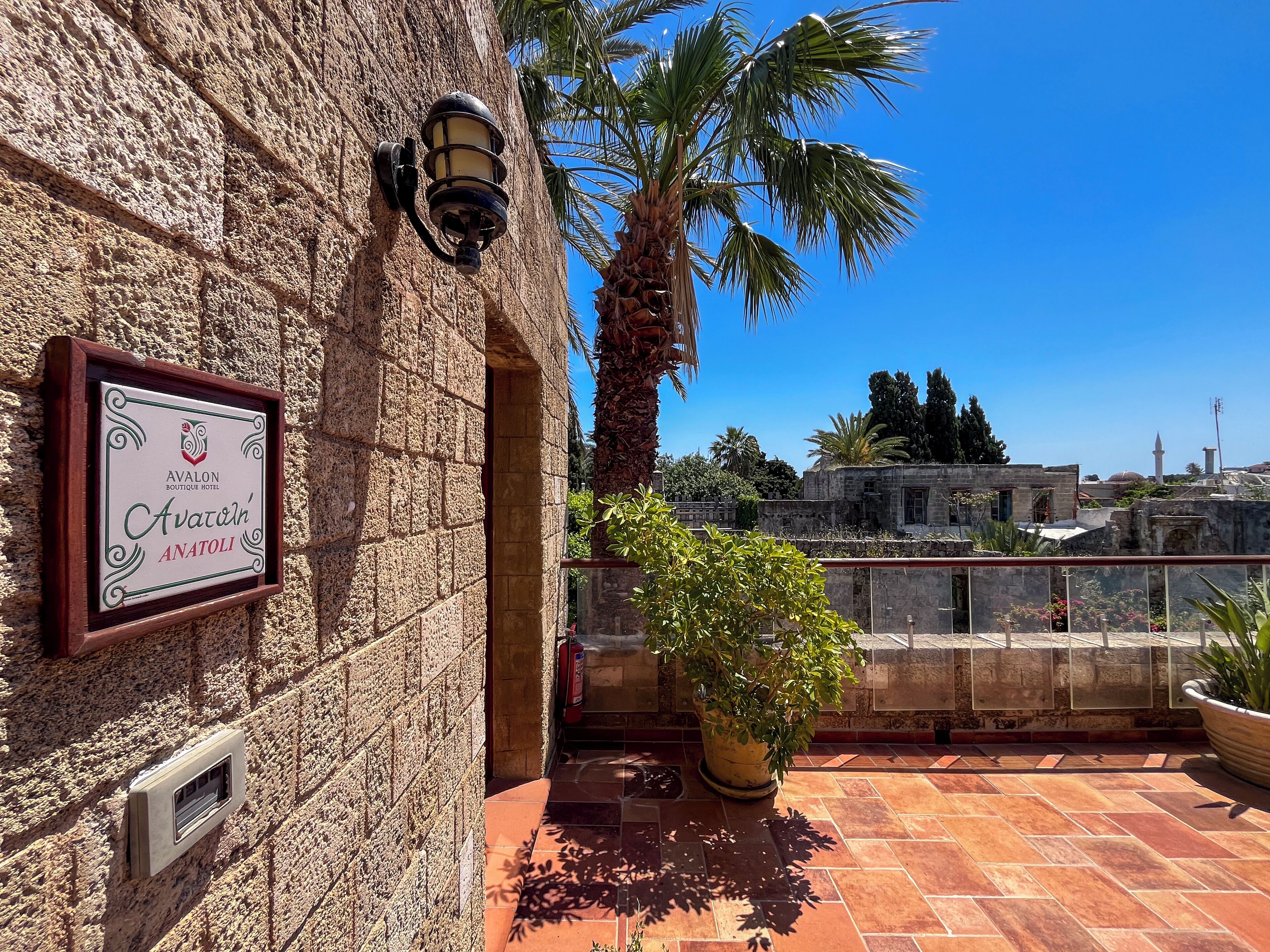 A stone wall with a framed sign for the Avalon Boutique Hotel in Anatolia, a potted plant, and a tiled patio area.