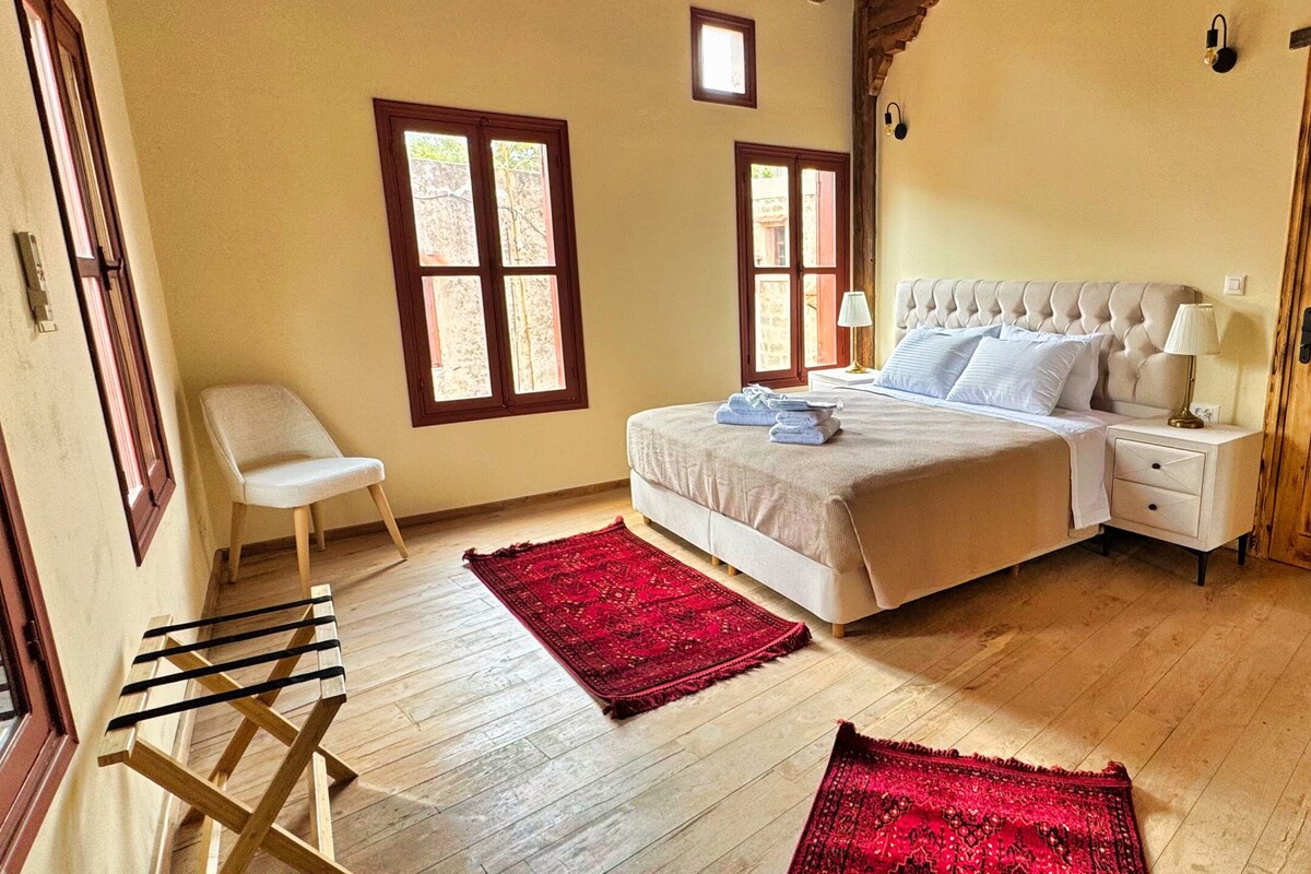Ein Schlafzimmer mit einem Bett, zwei Nachttischen, einem Sessel, einem Holzschrank und zwei Fenstern.