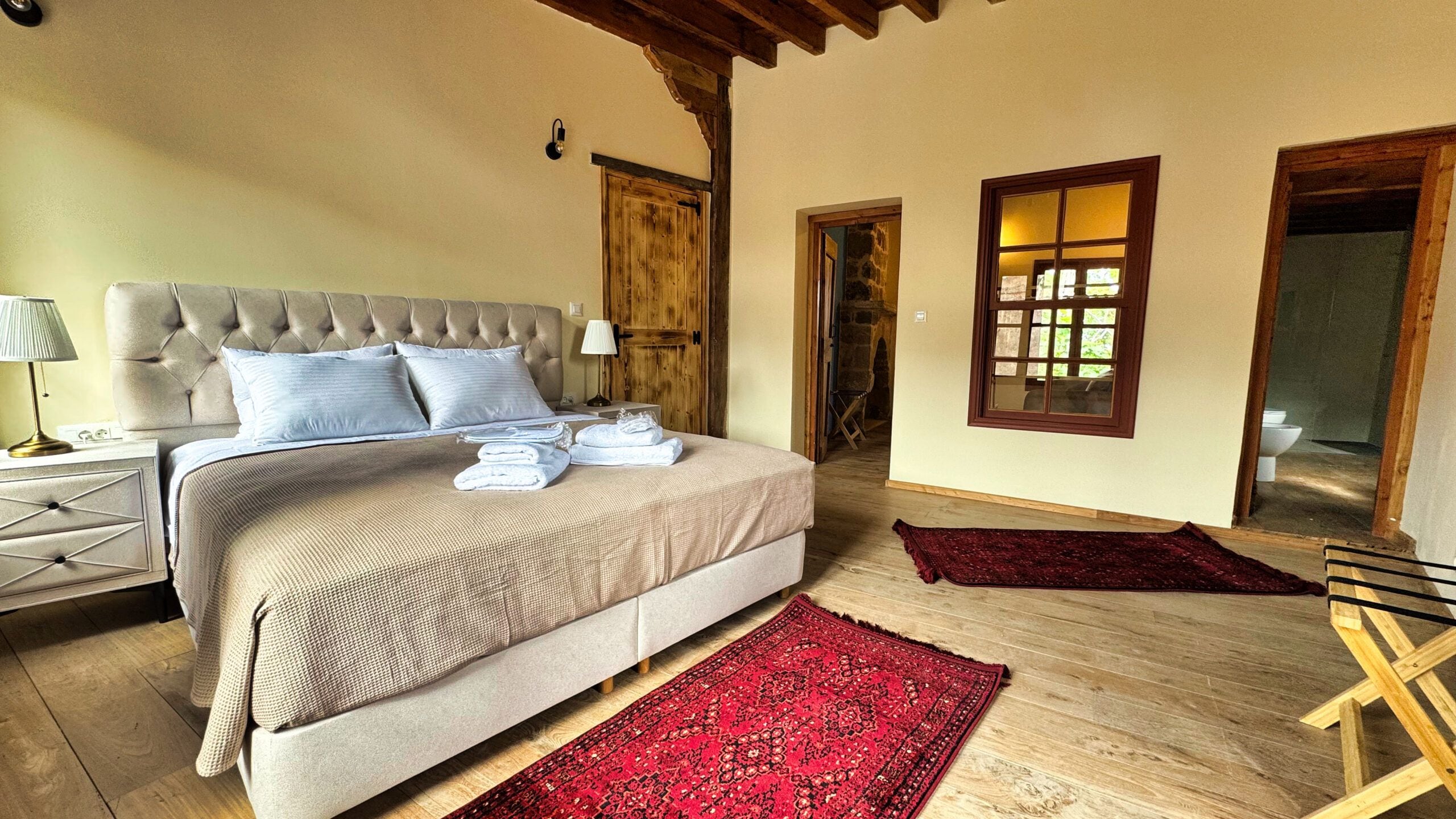 Une chambre avec un grand lit, des poutres en bois, un tapis rouge et une porte en bois.