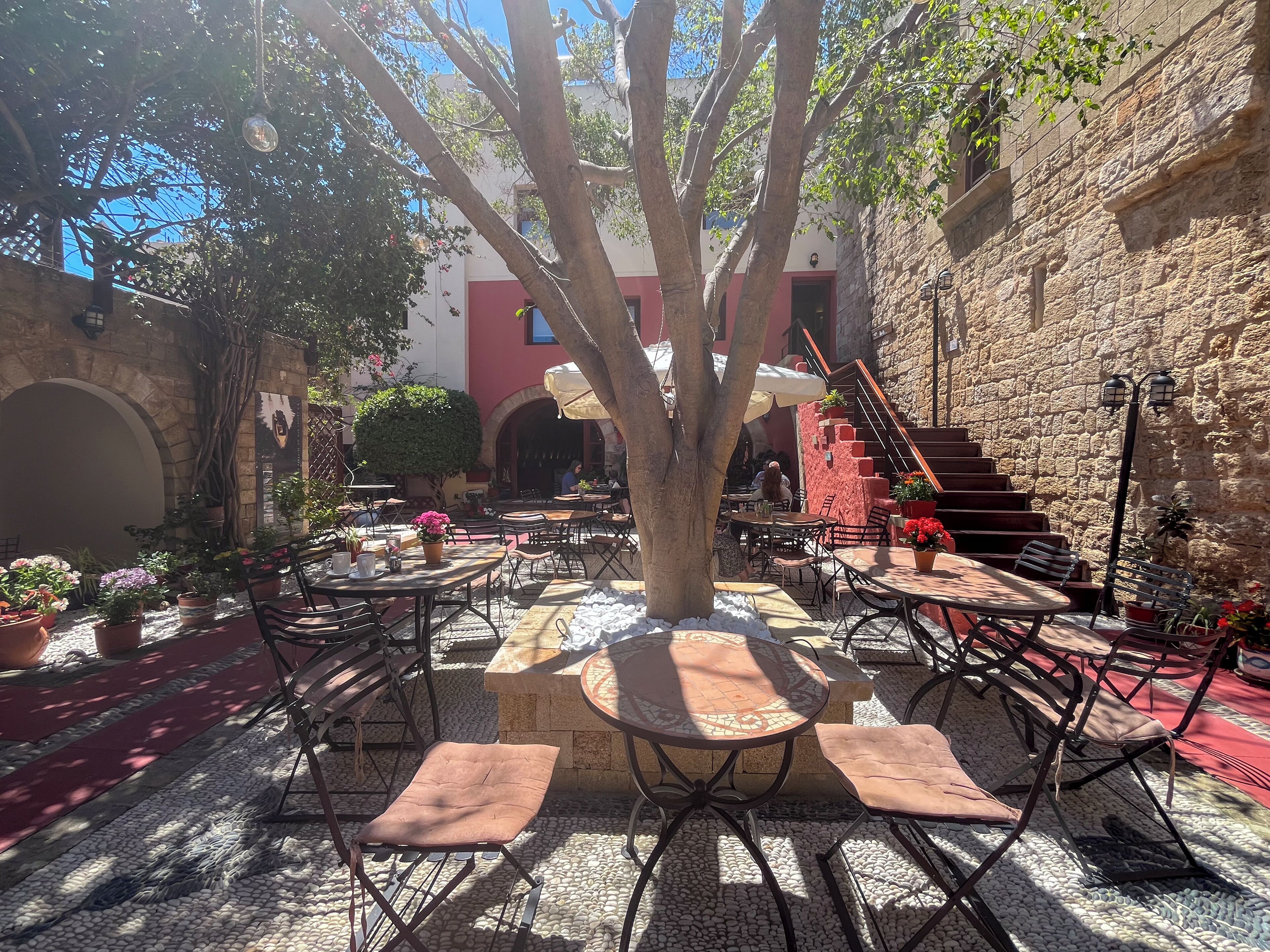 An outdoor patio area with tables and chairs, surrounded by stone walls and potted plants.