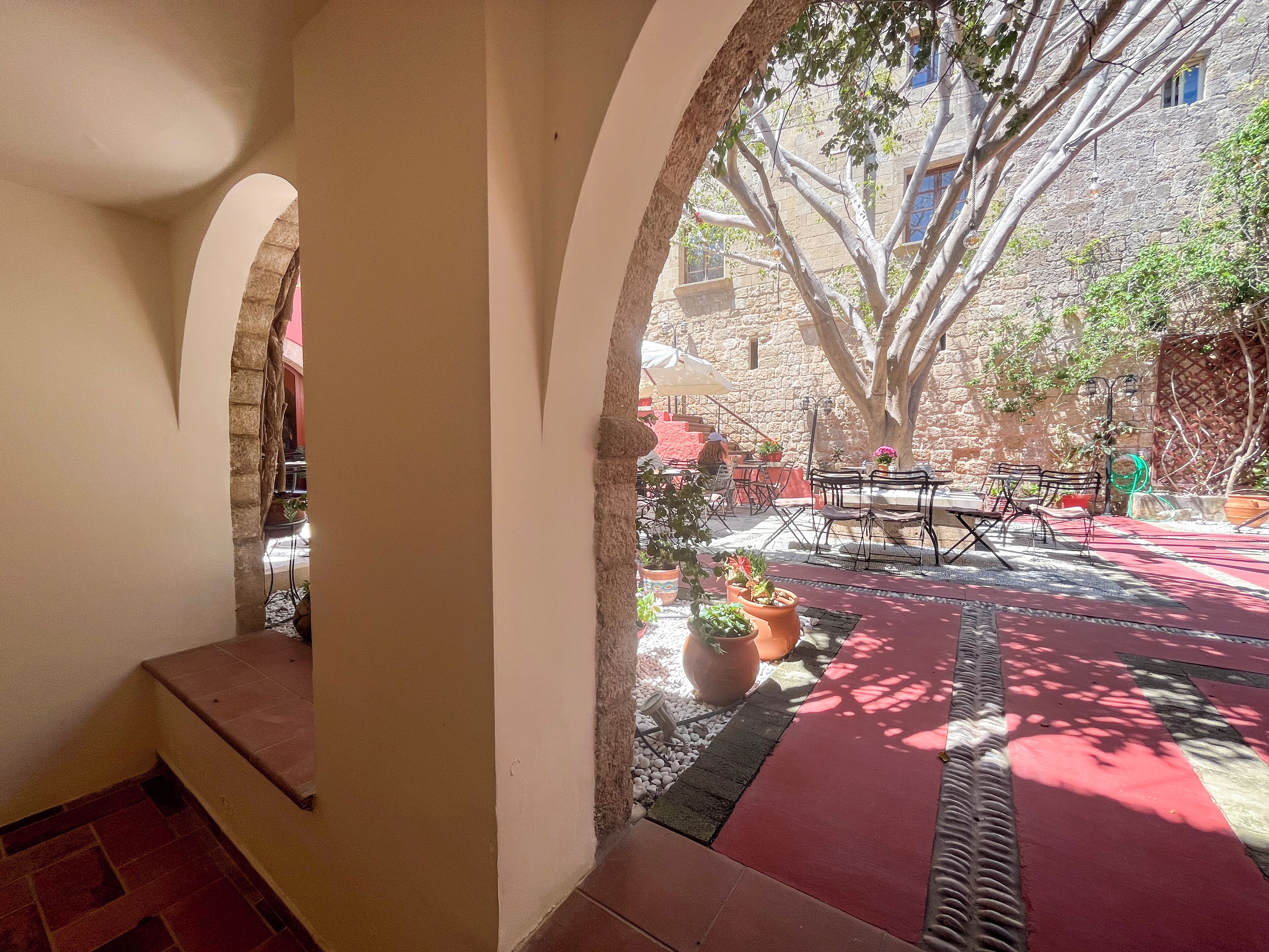 Un espace extérieur aménagé en terrasse, avec des murs en pierre, un sol rouge et des plantes en pot.