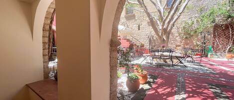 Un espace extérieur aménagé en terrasse, avec des murs en pierre, un sol rouge et des plantes en pot.