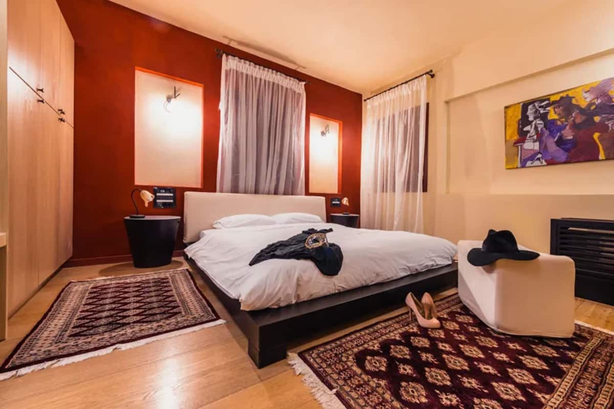 A modern bedroom with a large bed, two bedside tables, a nightstand, a chair, and a painting on the wall.