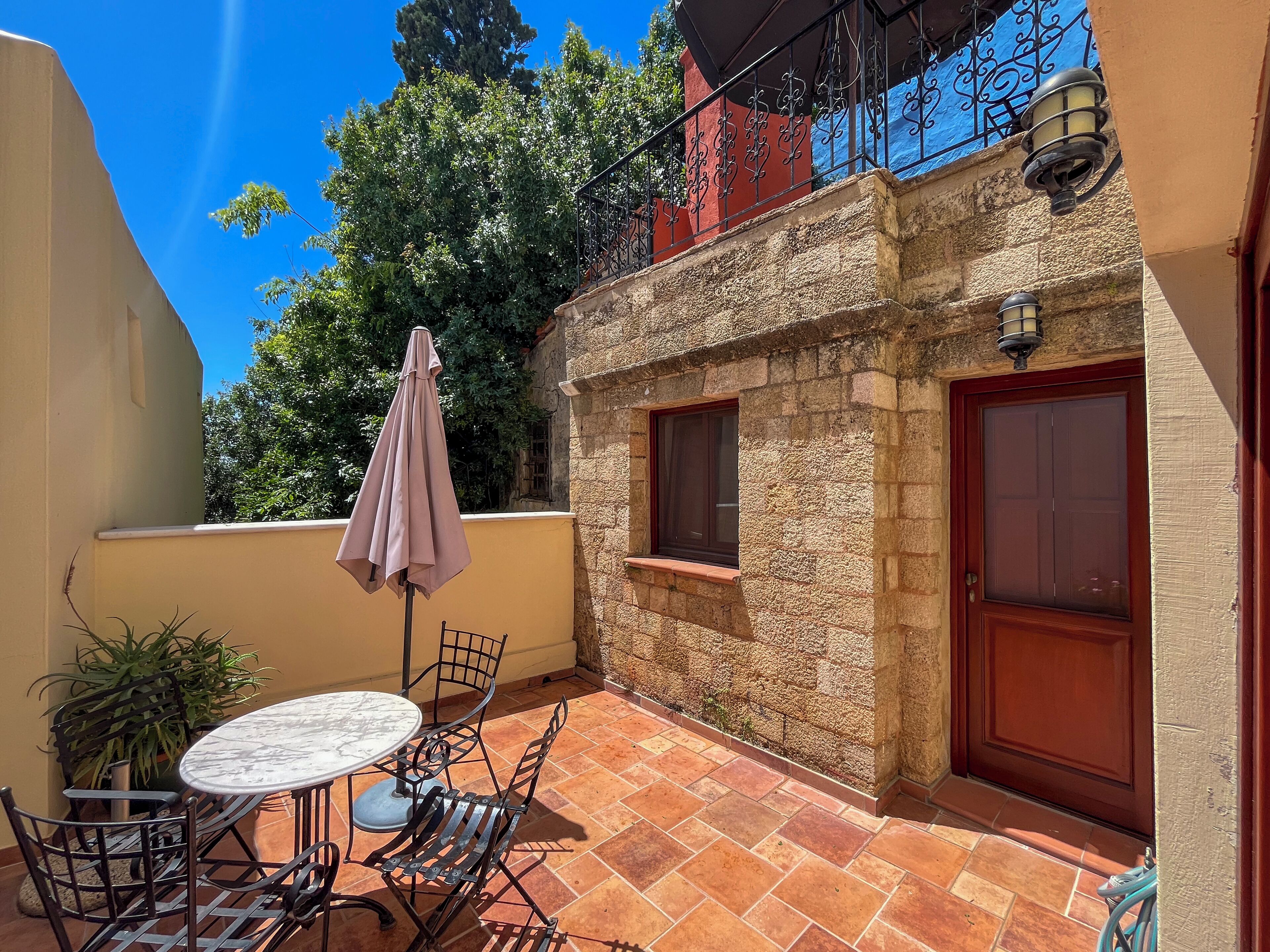 An outdoor patio with a round table and chairs, a potted plant, and a door.