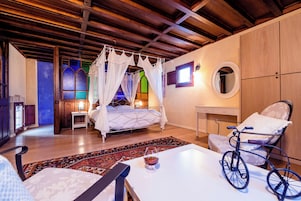Un dormitorio con cama con dosel, una silla de ruedas, una mesita de noche con lámpara y una ventana con vidrieras.