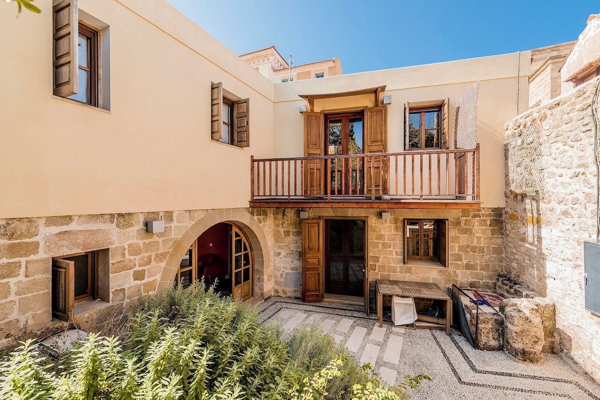 A courtyard with a stone wall, wooden doors, and a balcony with a railing.
