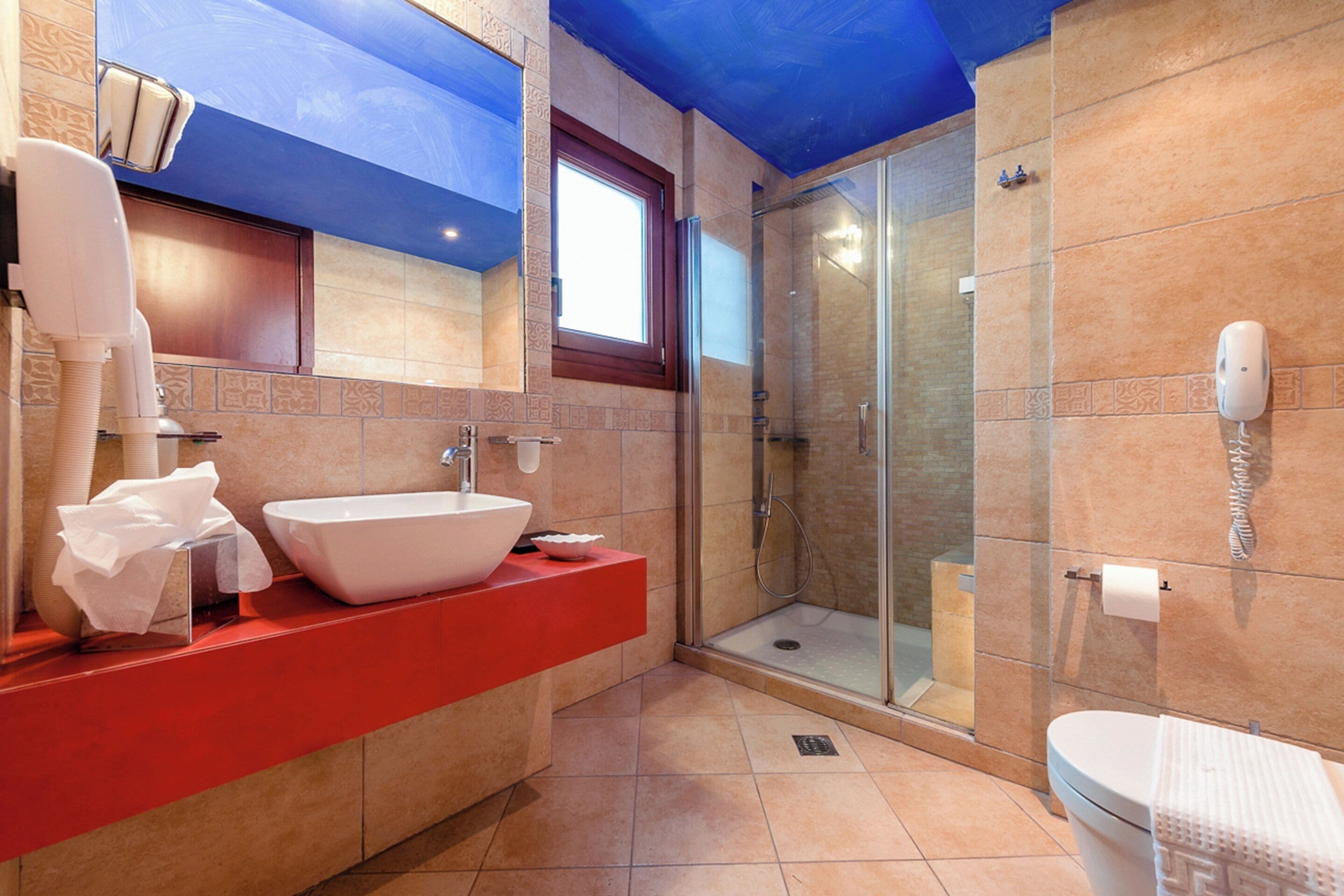 A modern bathroom with a large white sink, a glass shower enclosure, and a red countertop.