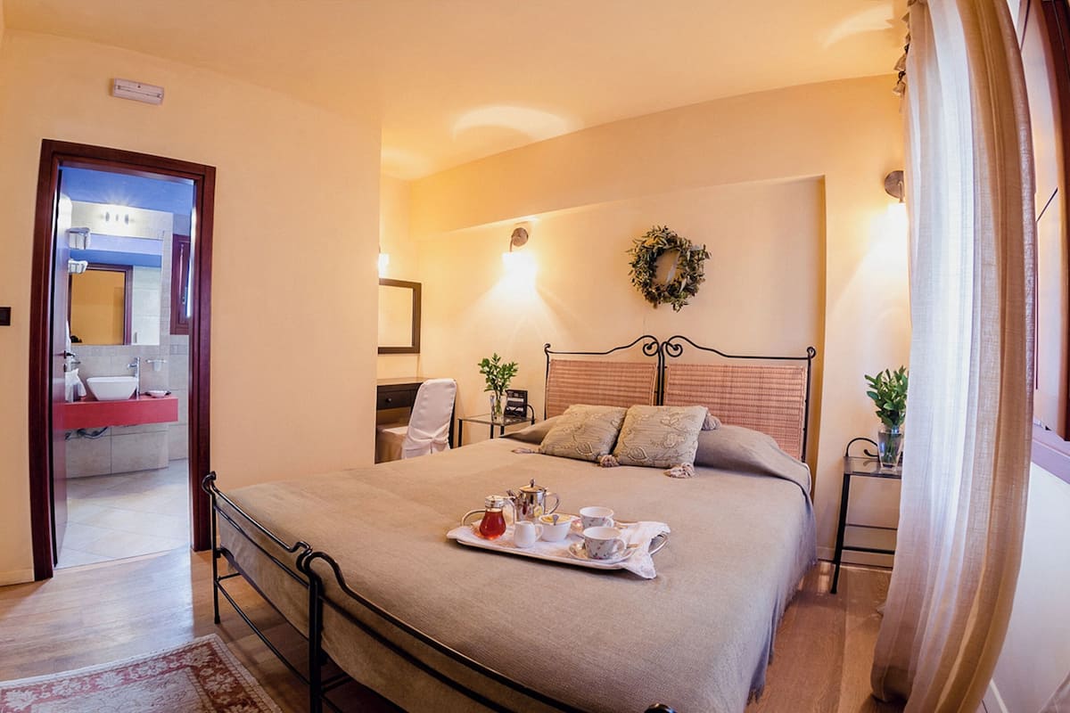 A neatly made bed with a tray of breakfast items, a bedside table with a plant, and a mirror in the adjacent room.