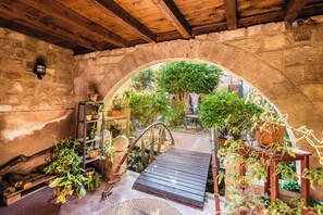 Un arcoado de piedra da acceso a un jardín con plantas en macetas y un banco de madera.