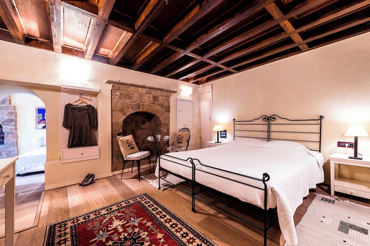 A bedroom with a stone fireplace, a bed, a nightstand, a chair, and a hanging garment.